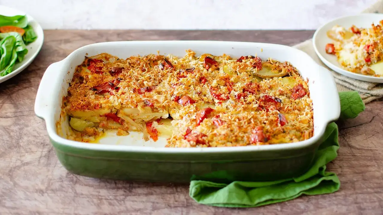 Parmigiana di patate dorata e croccante, con pomodorini e formaggio filante, servita in una teglia verde.