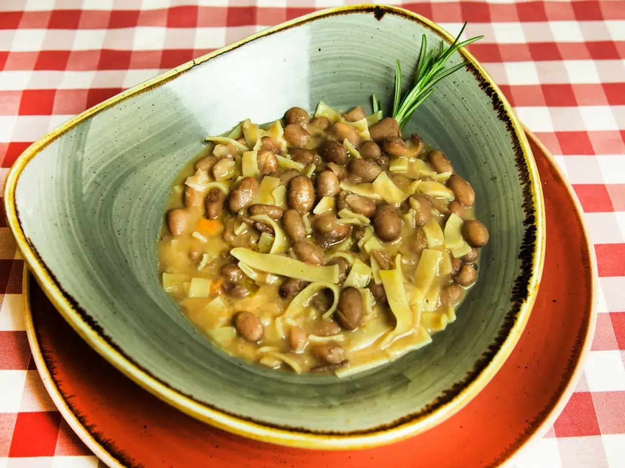 Un piatto fumante di pasta e fagioli, un classico confortante, guarnito con un rametto di rosmarino.