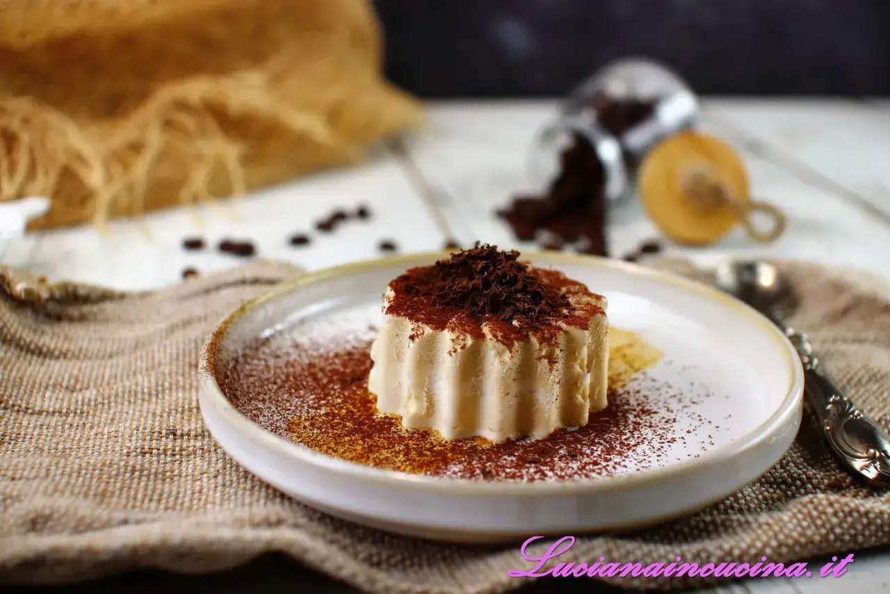 Delizioso semifreddo al caff&egrave;, spolverato di cacao e scaglie di cioccolato, su un piatto con chicchi di caff&egrave; sparsi.