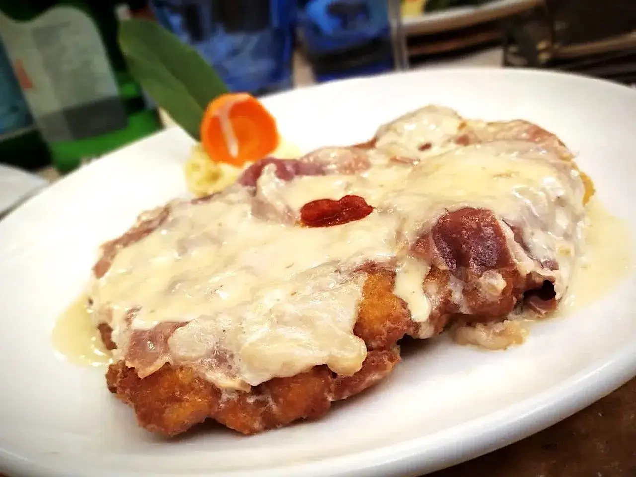 Cotoletta alla bolognese dorata e filante, con prosciutto e formaggio fuso, servita su un piatto bianco con contorno di pur&egrave; e carota.