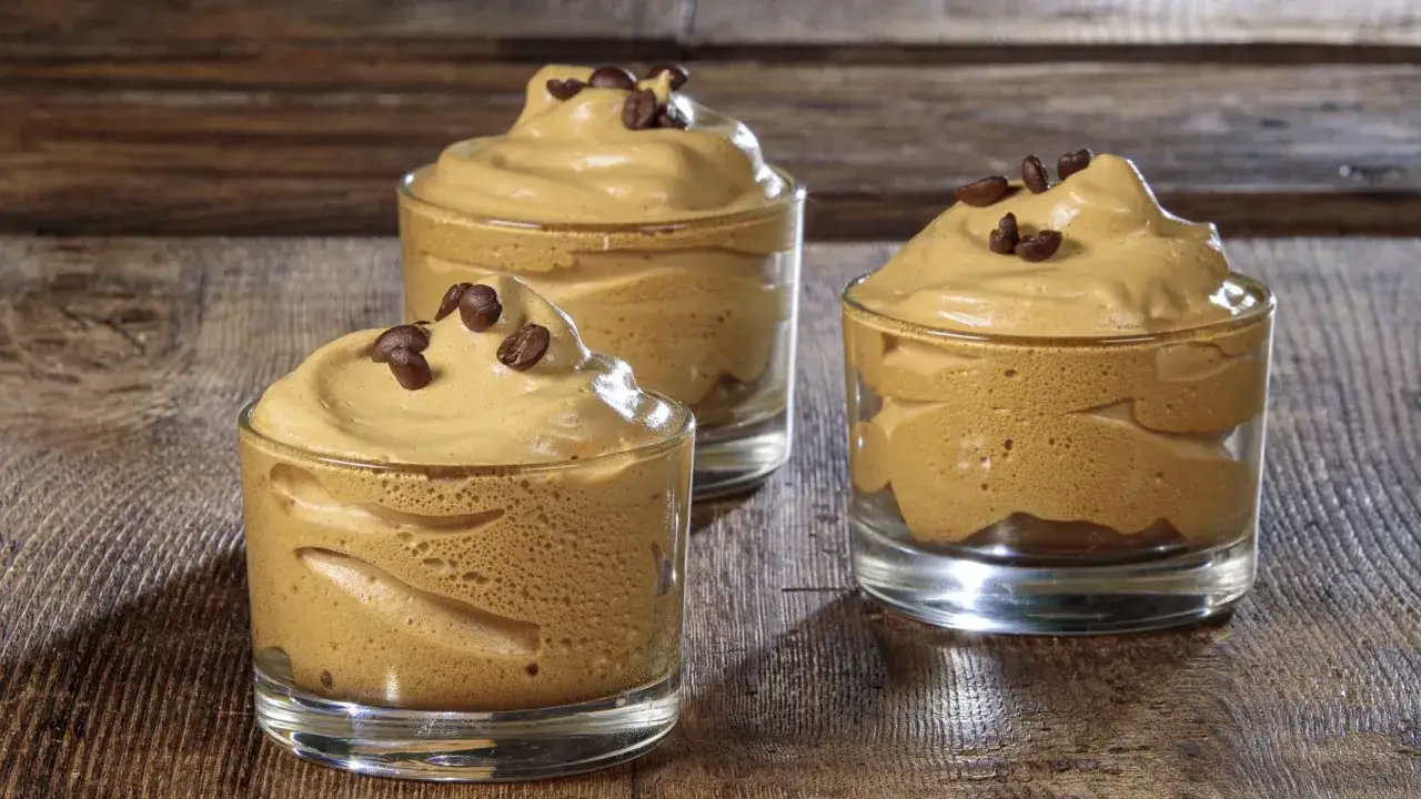 Tre bicchierini di crema di caff&egrave; senza panna, guarniti con chicchi di caff&egrave;, su un tavolo di legno.