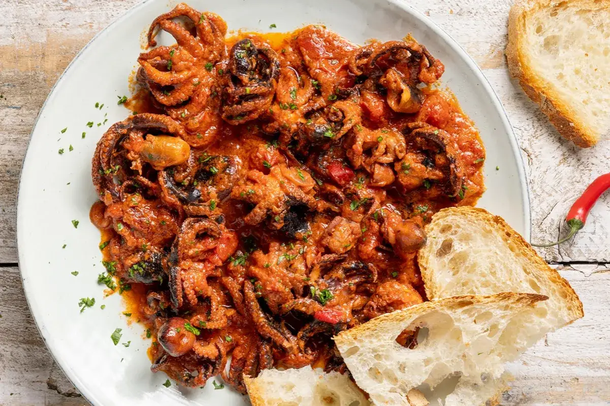 Polipetti in purgatorio, un piatto succulento con tentacoli teneri in salsa rossa, accompagnato da pane rustico e un peperoncino piccante.