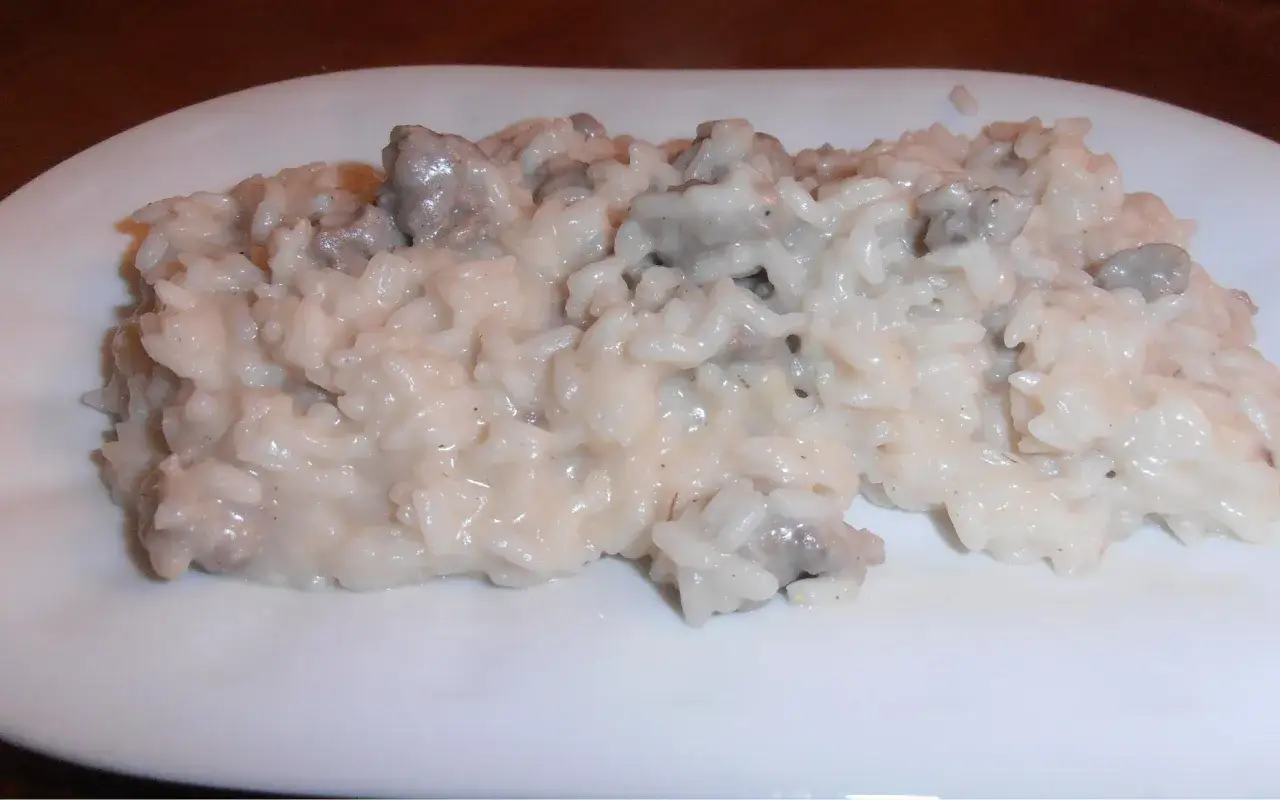 Un cremoso risotto con salsiccia, servito su un piatto bianco.