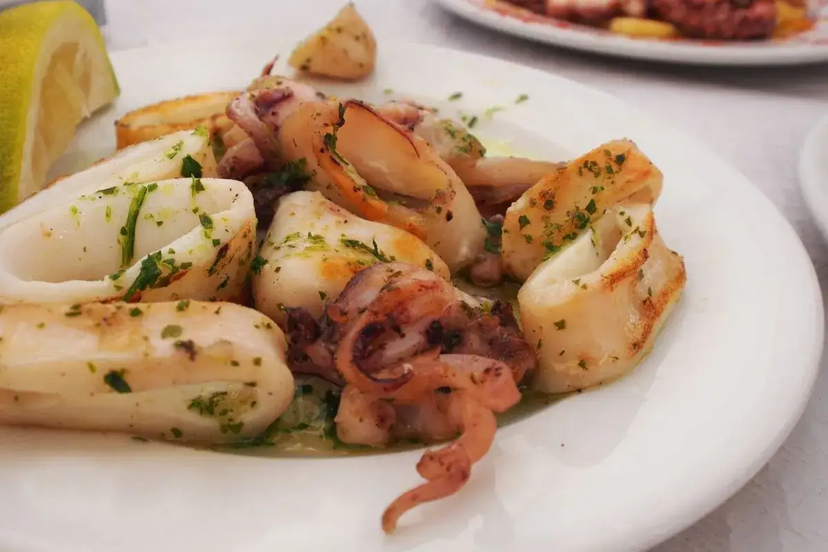 Calamari in padella, succulenti e dorati, conditi con prezzemolo fresco e serviti con uno spicchio di limone.