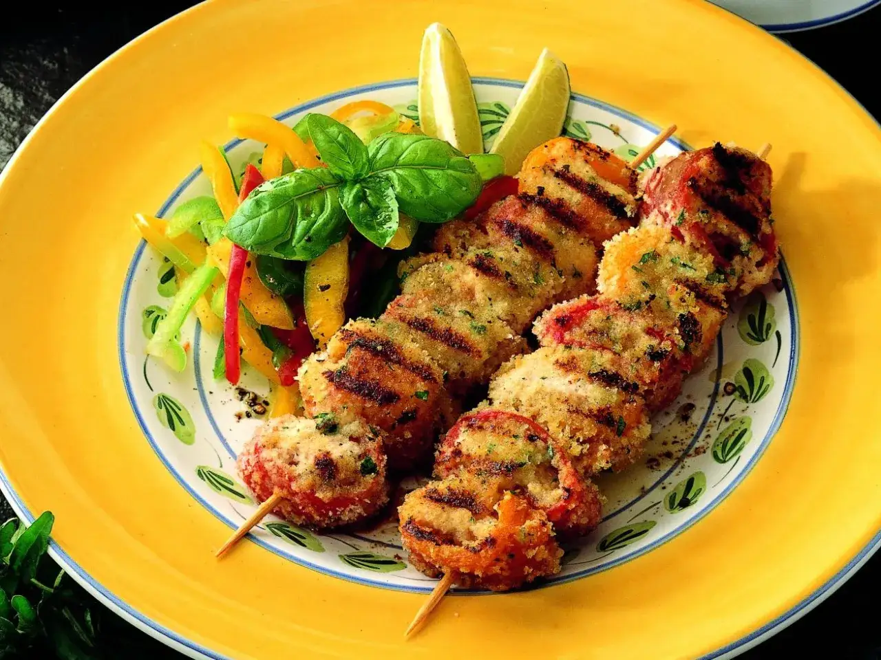 Spiedini di pesce impanati e grigliati, serviti con un'insalata colorata di peperoni e basilico fresco.