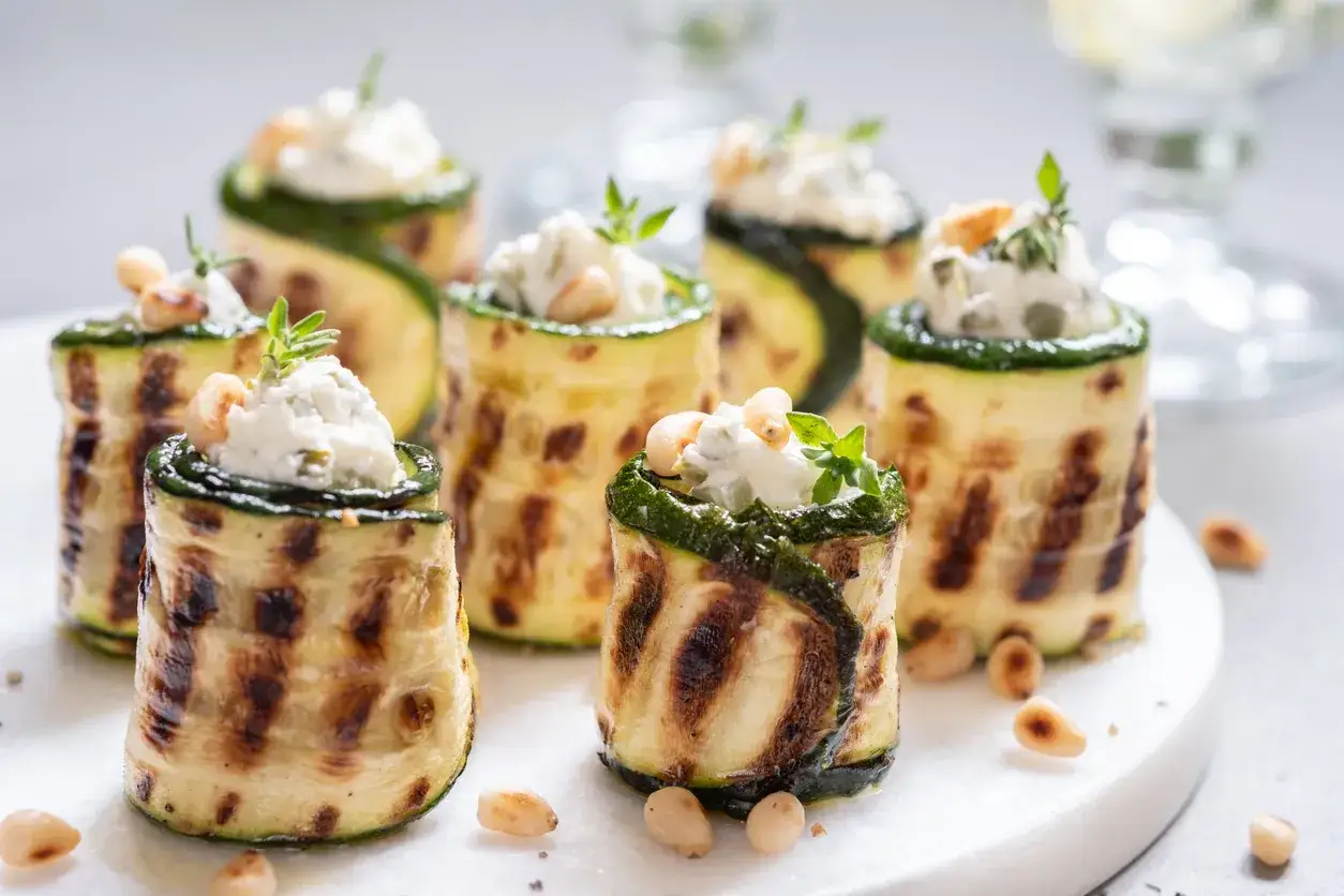 Deliziosi involtini di zucchine grigliate ripieni di formaggio cremoso, guarniti con pinoli e erbe aromatiche.