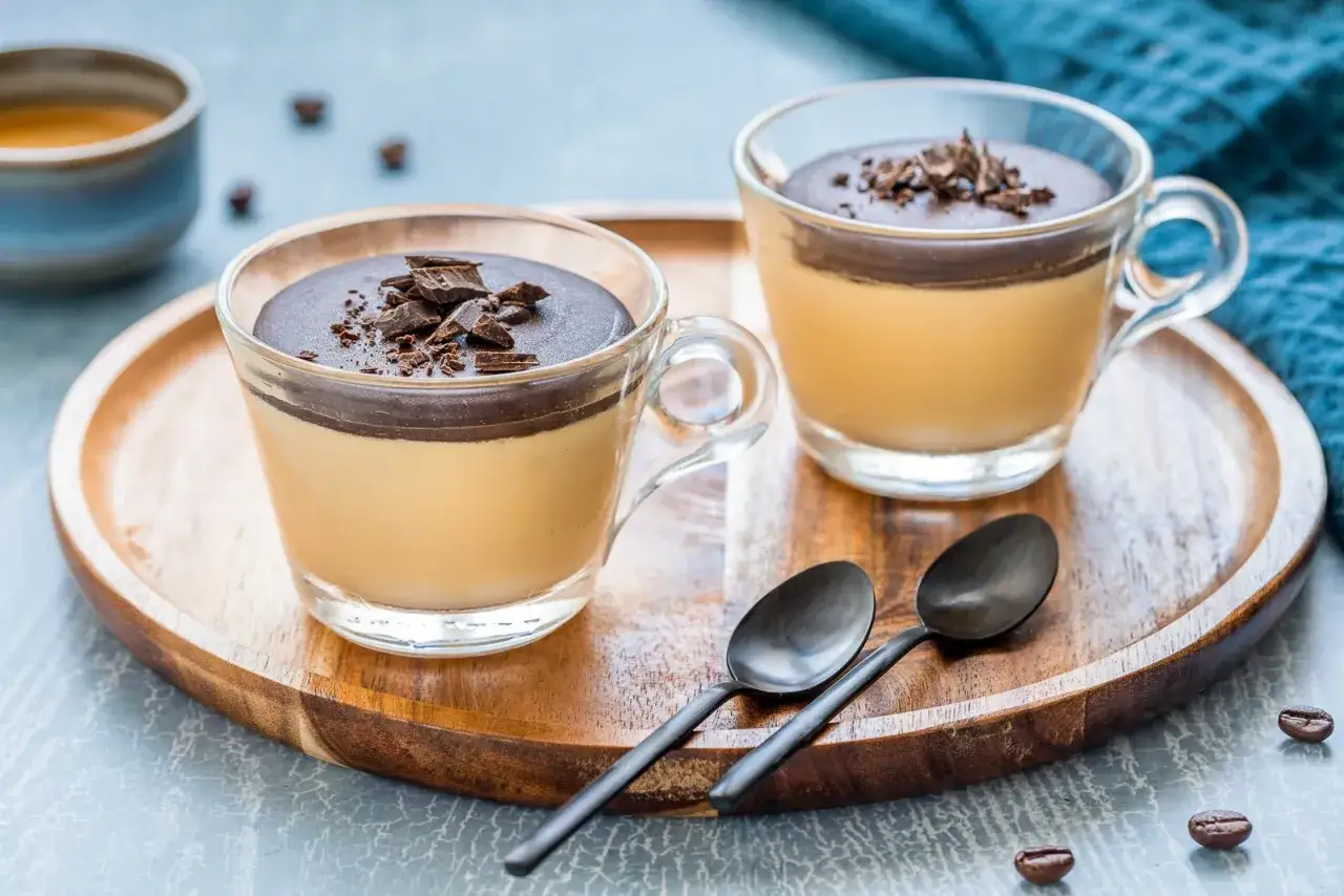 Delizioso spumone al caff&egrave; con copertura di cioccolato fondente e scaglie croccanti, servito in coppette di vetro su un vassoio di legno.