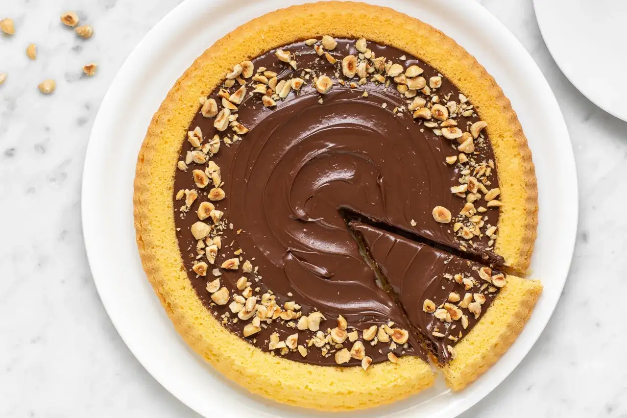 Deliziosa crostata alla Nutella con bordo dorato e nocciole tritate, una fetta &egrave; gi&agrave; stata servita.