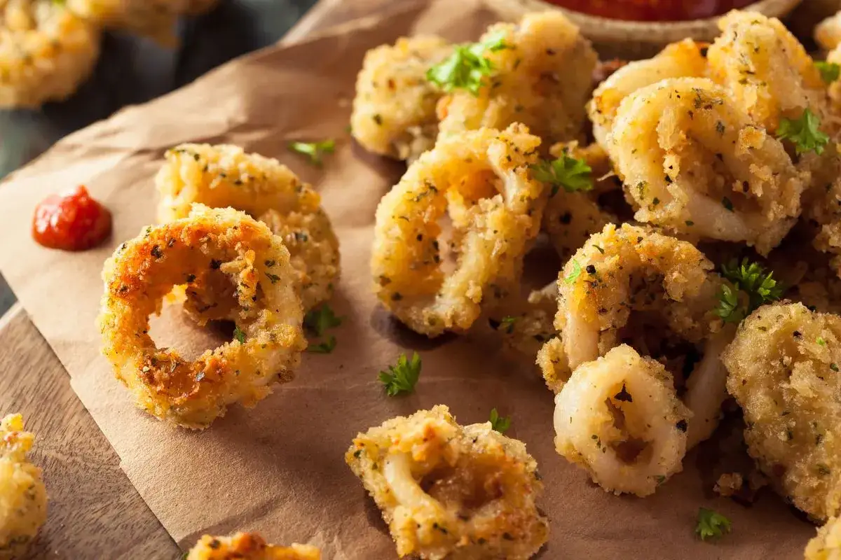 Anelli dorati e croccanti di calamari gratinati al forno, guarniti con prezzemolo fresco e accompagnati da una salsa rossa.