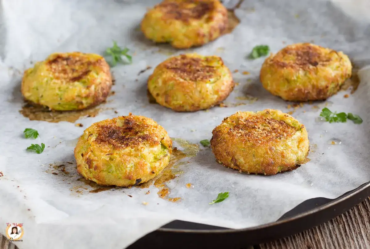 Sei polpette di zucchine dorate e croccanti su carta forno, guarnite con prezzemolo fresco.