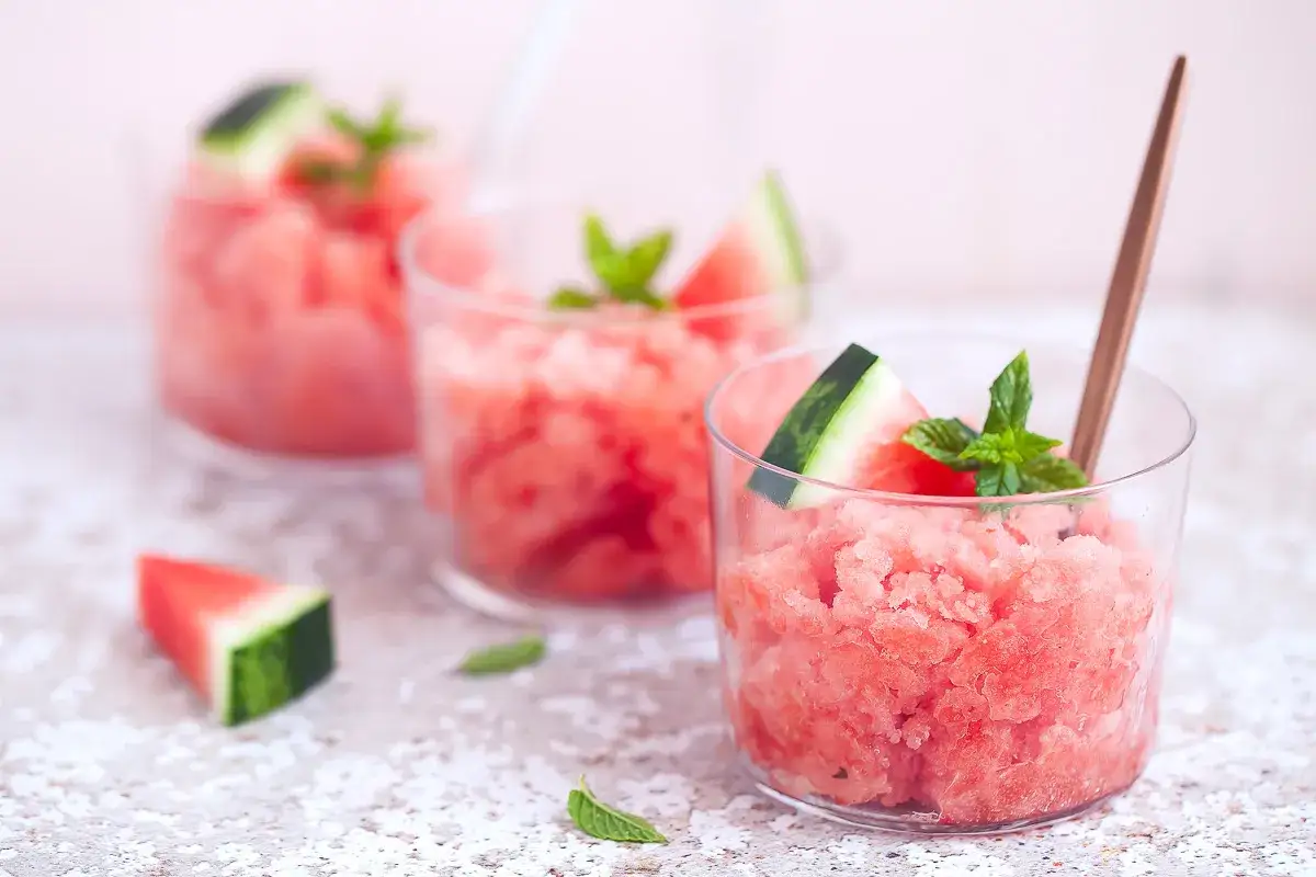 Tre bicchieri di rinfrescante granita di anguria, guarniti con spicchi di frutta e menta fresca. Perfetta per un'estate golosa.