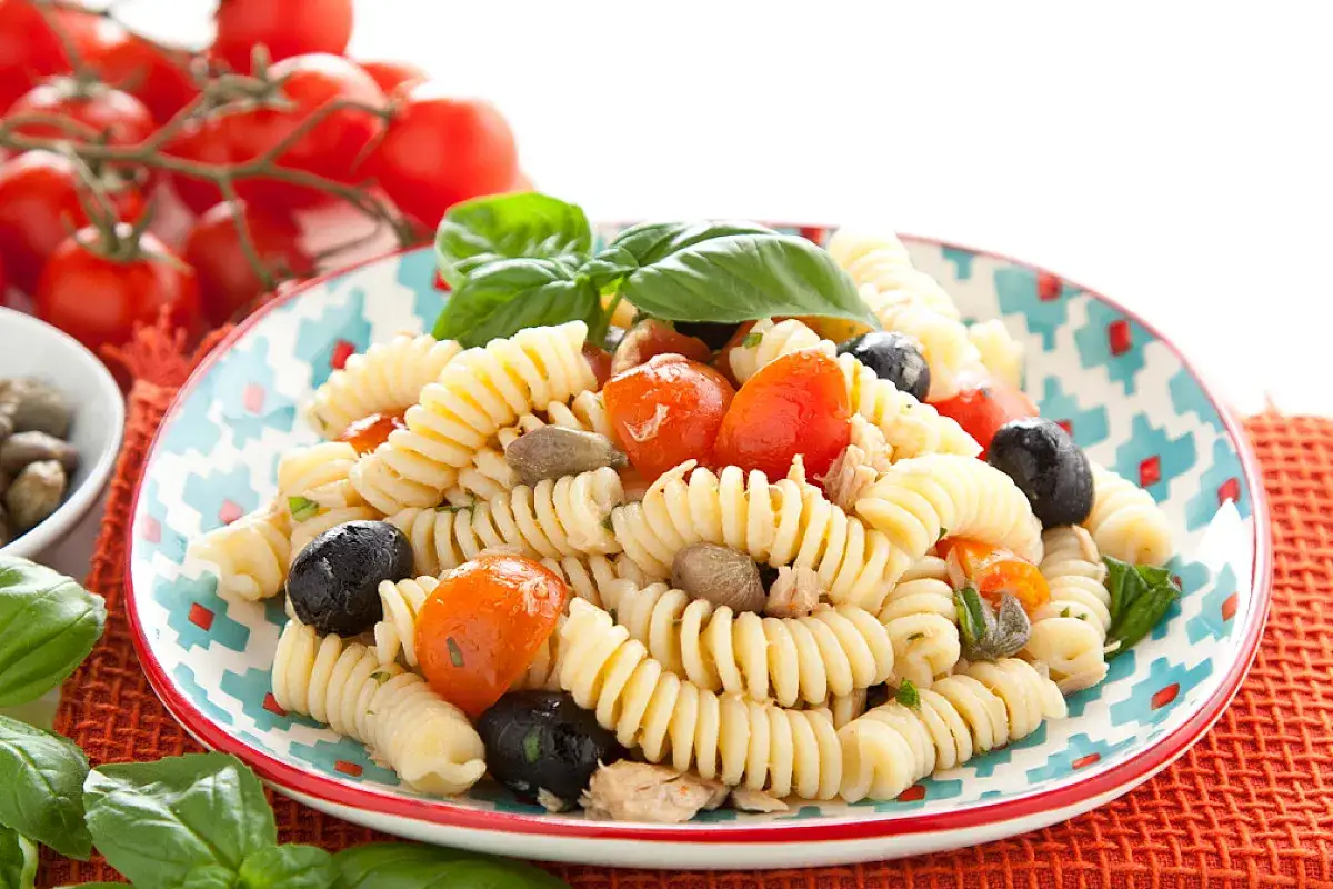 Fusilli con pomodorini, olive nere, capperi e tonno, un'insalata di tonno fresca e colorata, guarnita con basilico.