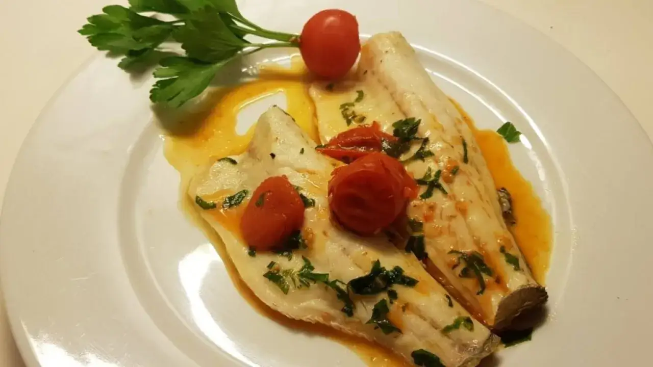 Filetti di branzino in padella, succulenti e profumati, con pomodorini e prezzemolo fresco.