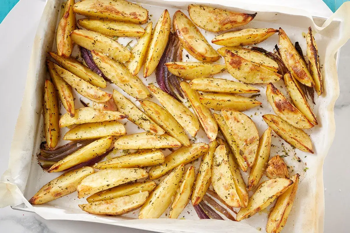 Patate al forno croccanti, dorate e condite con erbe aromatiche, disposte su una teglia foderata di carta da forno.