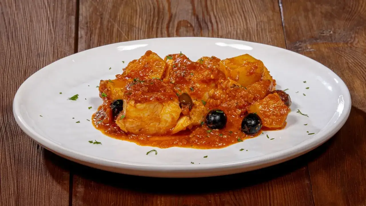 Piatto di baccal&agrave; in umido con patate e olive nere, guarnito con prezzemolo tritato.