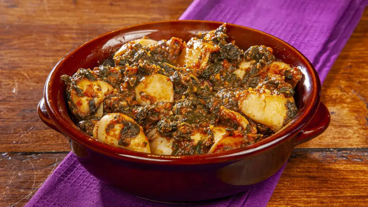Un saporito piatto di seppie in zimino, cotte lentamente con verdure e pomodoro, servite in una ciotola di terracotta su un tovagliolo viola.