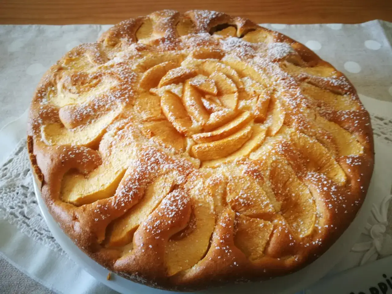 Torta di mele senza glutine decorata con mele a forma di rosa e spolverata di zucchero a velo.