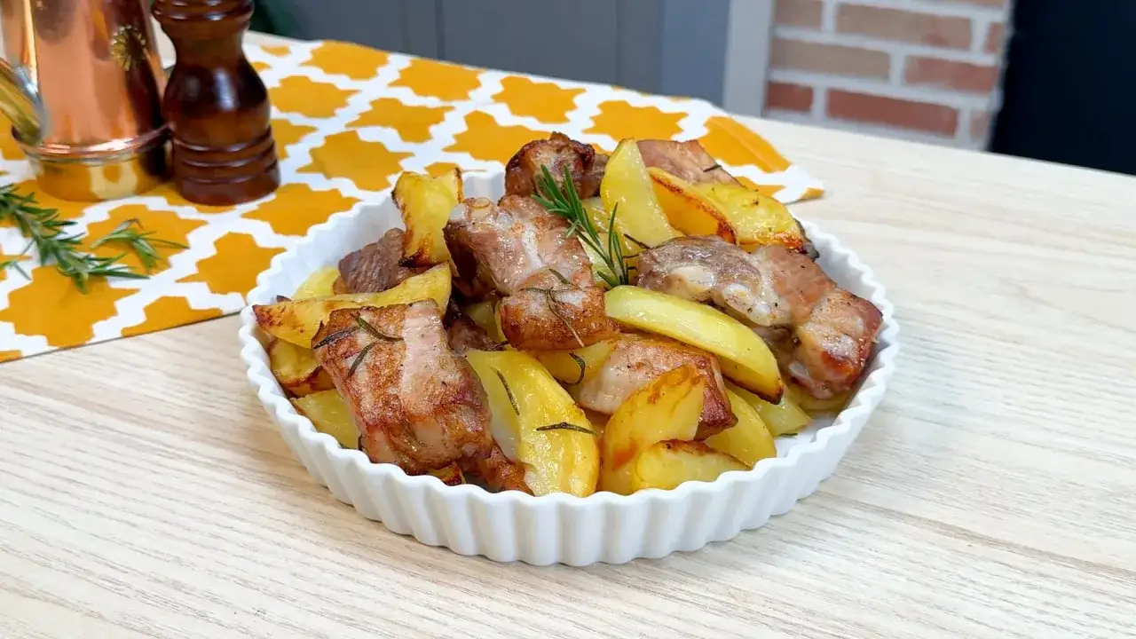 Succulente costine al forno con patate dorate, profumate al rosmarino, servite in una ciotola bianca.