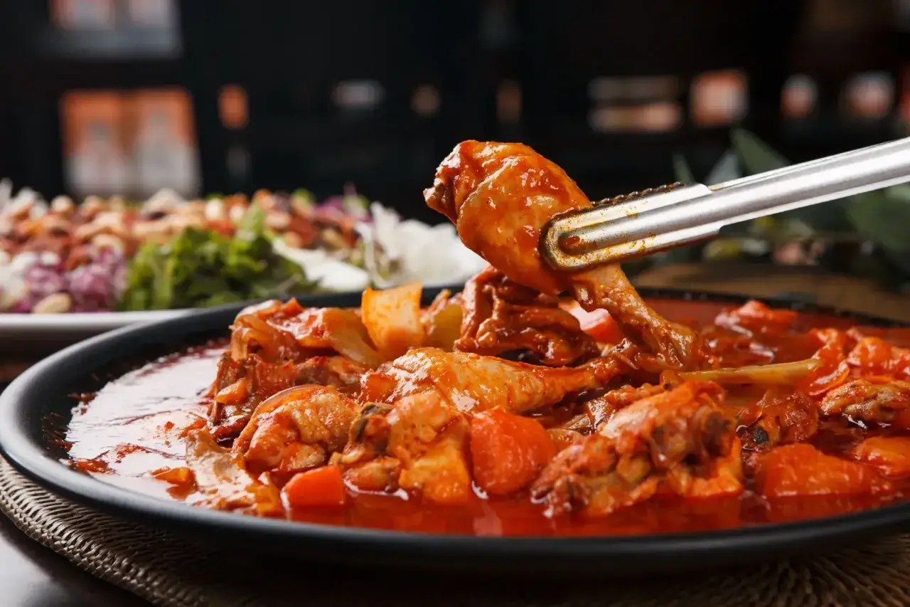 Un delizioso friccò di pollo in salsa rossa, con pezzi di pollo succulenti e verdure, servito in un piatto scuro.