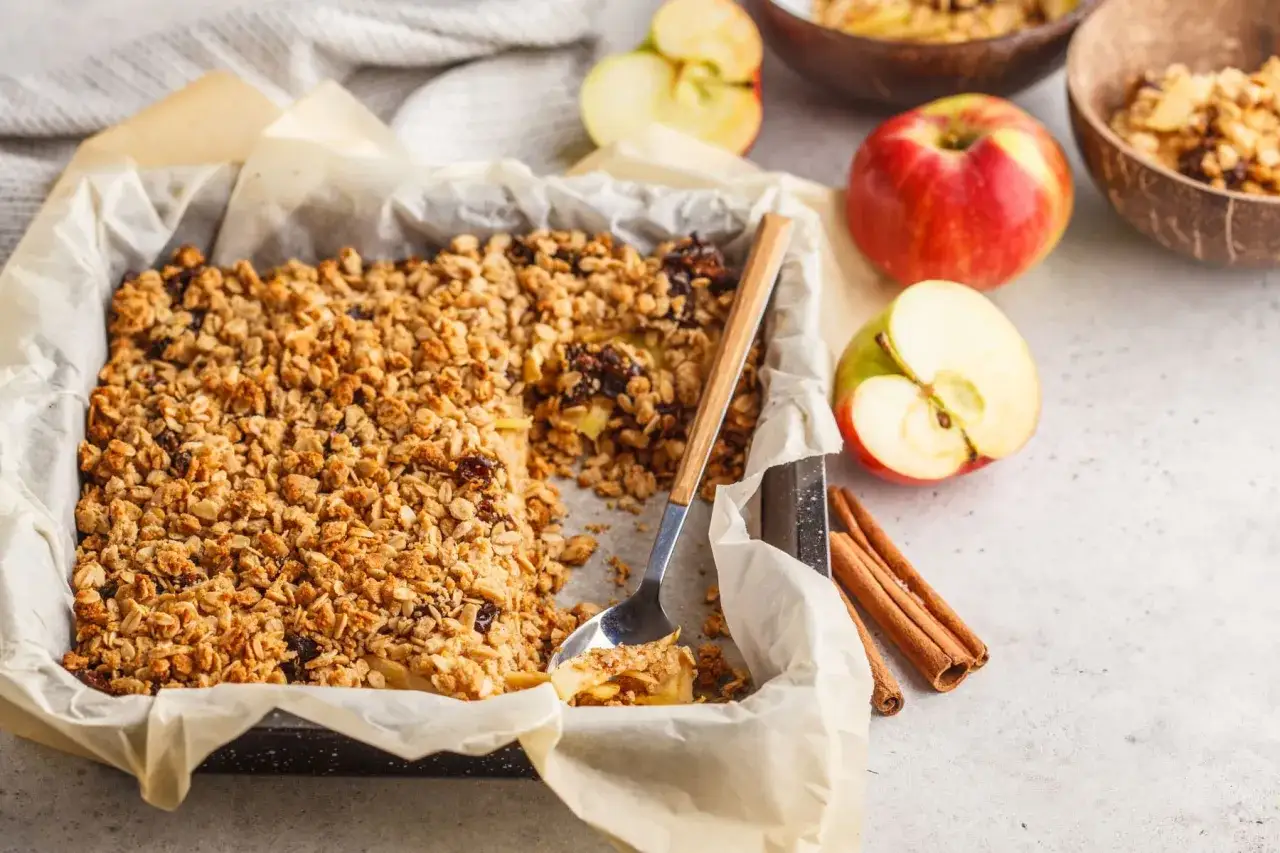 Un delizioso crumble di mele appena sfornato, con mele fresche e cannella a lato.