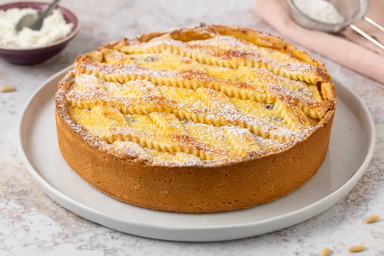 Deliziosa crostata di ricotta con una griglia dorata e una spolverata di zucchero a velo, pronta per essere gustata.