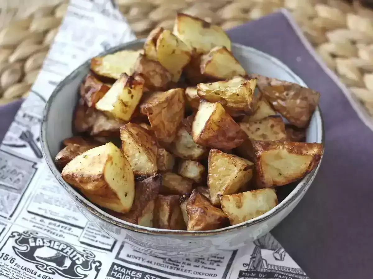 Patate lesse in friggitrice ad aria, dorate e croccanti, servite in una ciotola su carta di giornale.