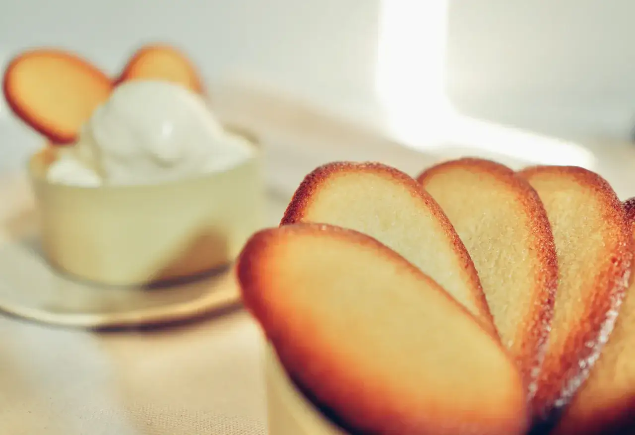 Biscotti a forma di lingue di gatto, dorati e croccanti, accanto a una ciotola con panna montata.