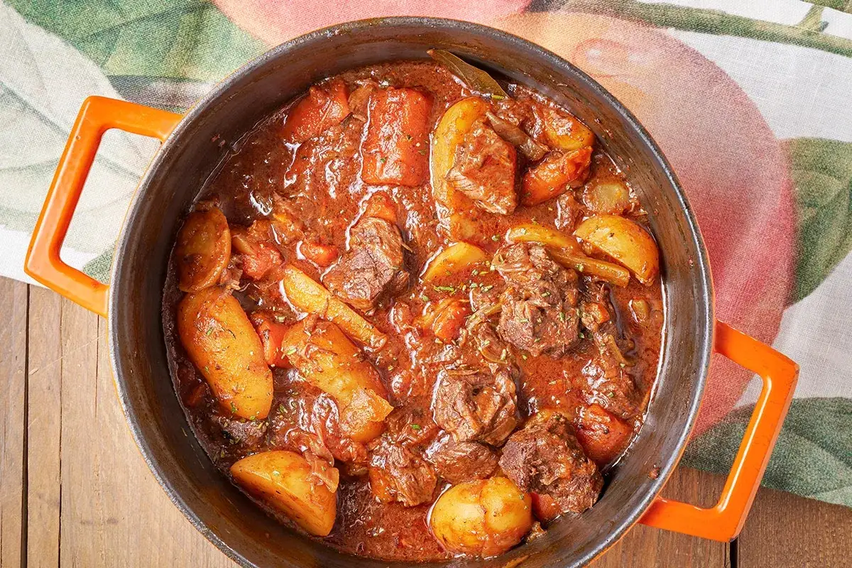 Un saporito spezzatino di manzo con patate e carote, cotto lentamente in una casseruola arancione.