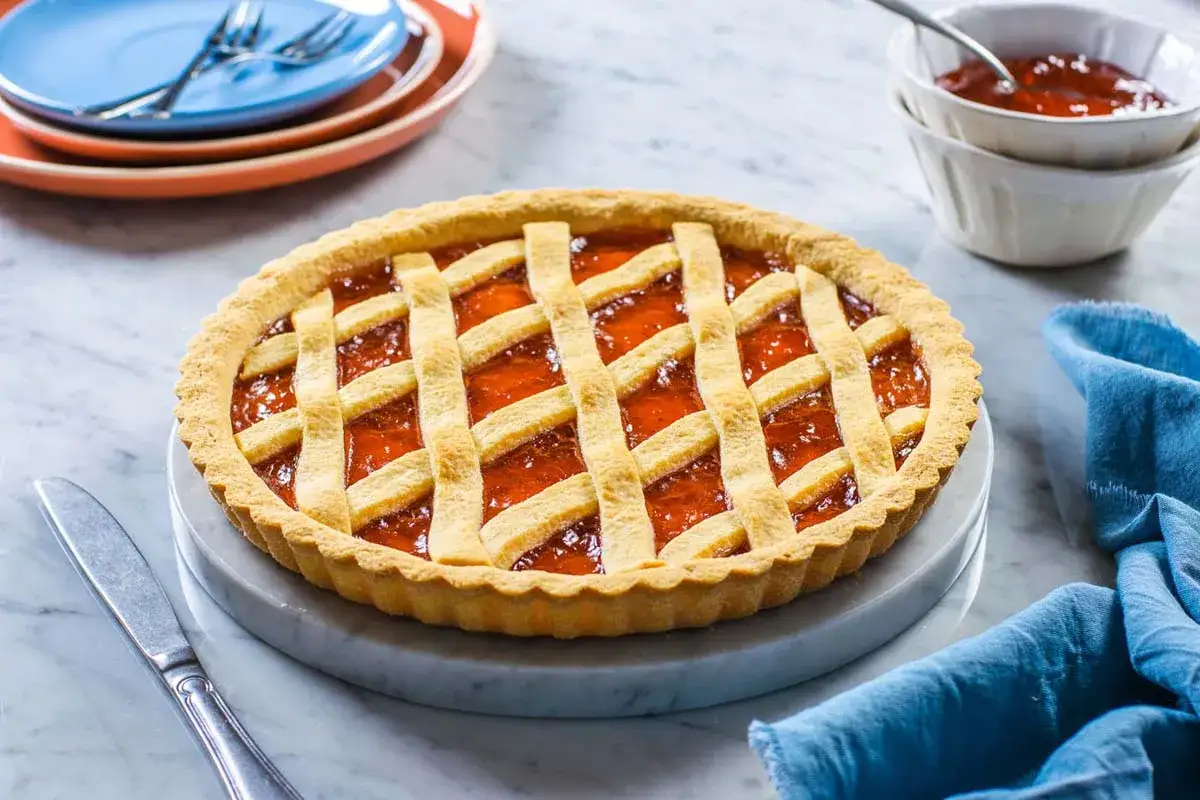 Deliziosa crostata senza glutine con marmellata di albicocche, decorata con una griglia di pasta frolla dorata. Perfetta per ogni occasione.