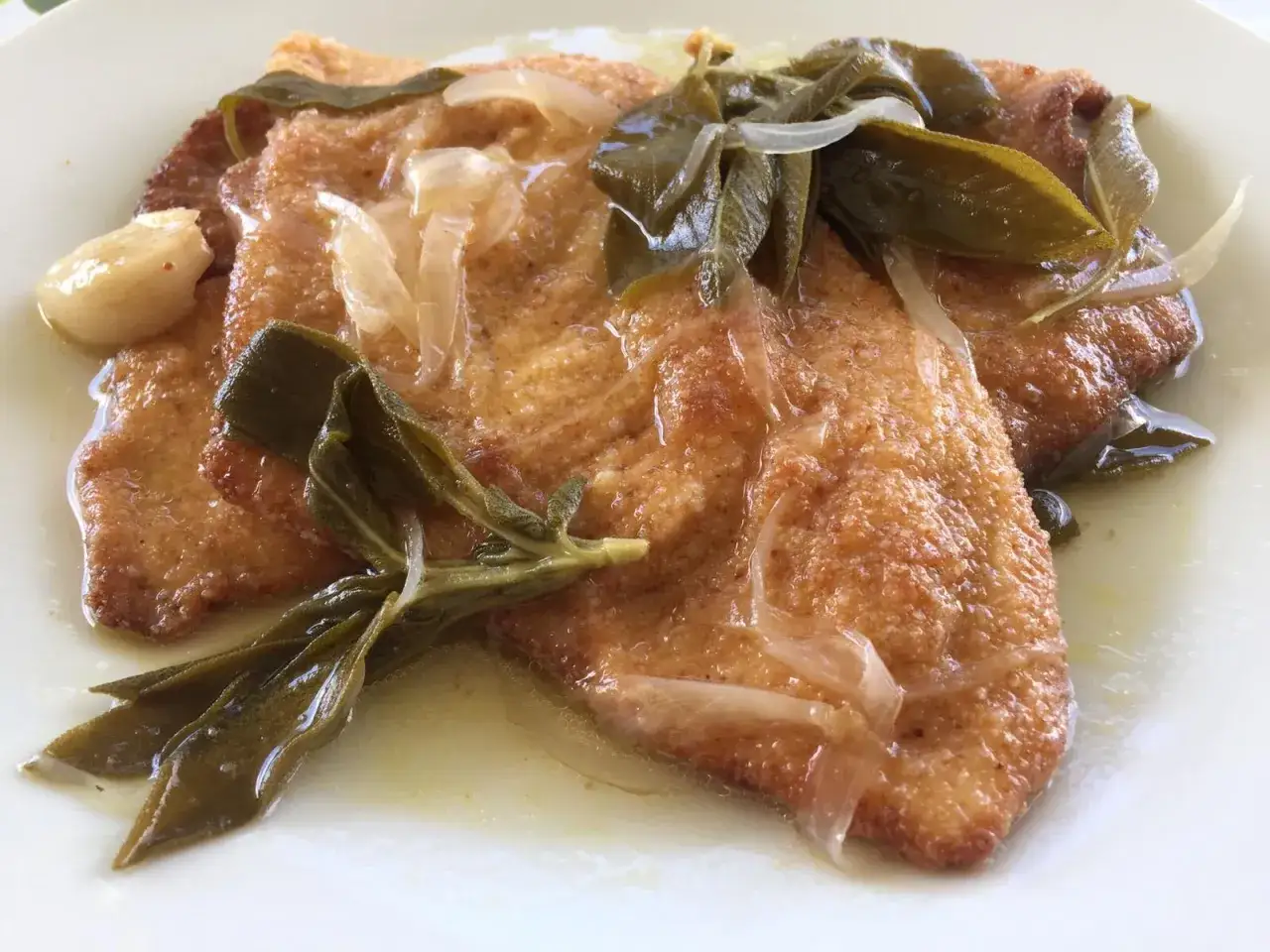 Delizioso pollo in carpione con cipolle, salvia e aglio, servito su un piatto bianco.