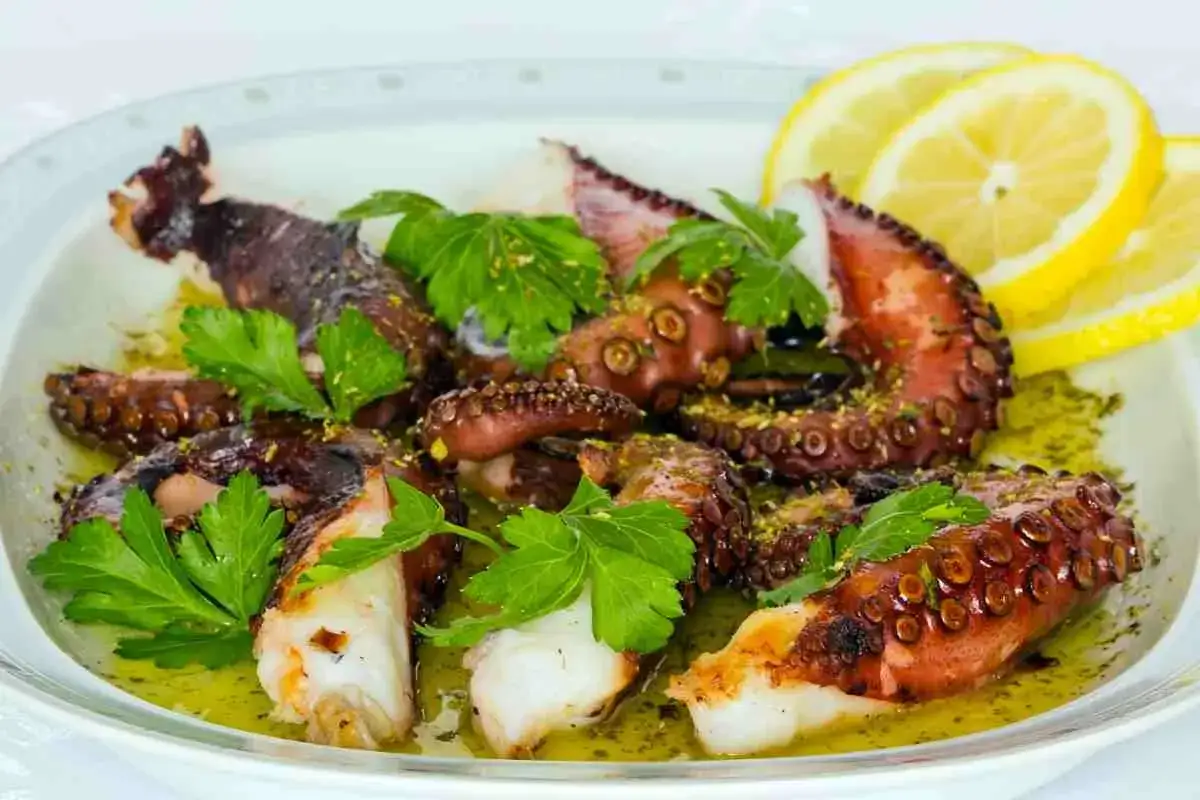 Delizioso polpo alla griglia, tenero e saporito, servito con prezzemolo fresco e spicchi di limone.