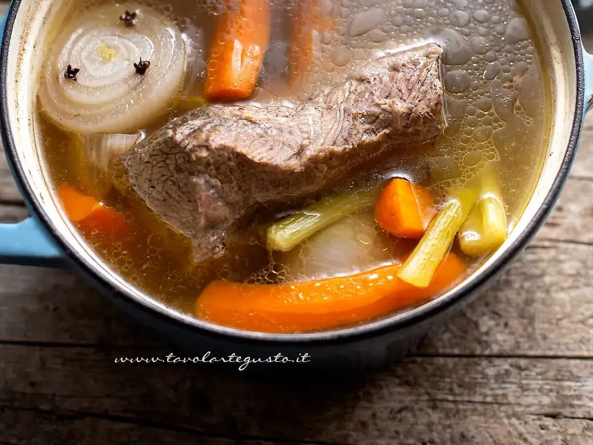 Un pezzo di carne succulenta cuoce lentamente in un brodo di carne ricco, con carote, sedano e cipolla.