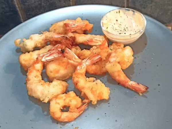 Gamberi in tempura dorati e croccanti, serviti su un piatto blu con una ciotolina di salsa cremosa.