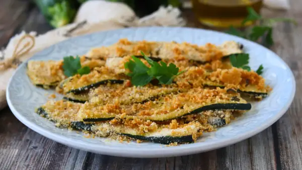 Fette di zucchine al forno, impanate e dorate, guarnite con prezzemolo fresco. Un contorno leggero e gustoso.