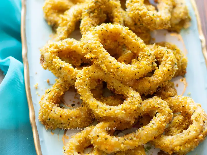 Anelli di totano al forno dorati e croccanti, serviti su un piatto azzurro con un tovagliolo turchese.