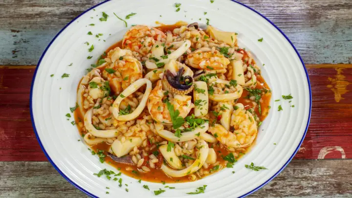 Un invitante risotto alla pescatora, ricco di gamberi, calamari e cozze, guarnito con prezzemolo fresco.