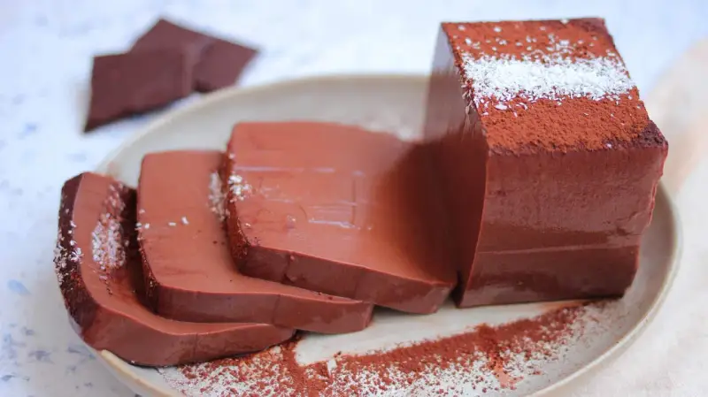 Fette di budino al cioccolato, spolverate di cacao e cocco, su un piatto.